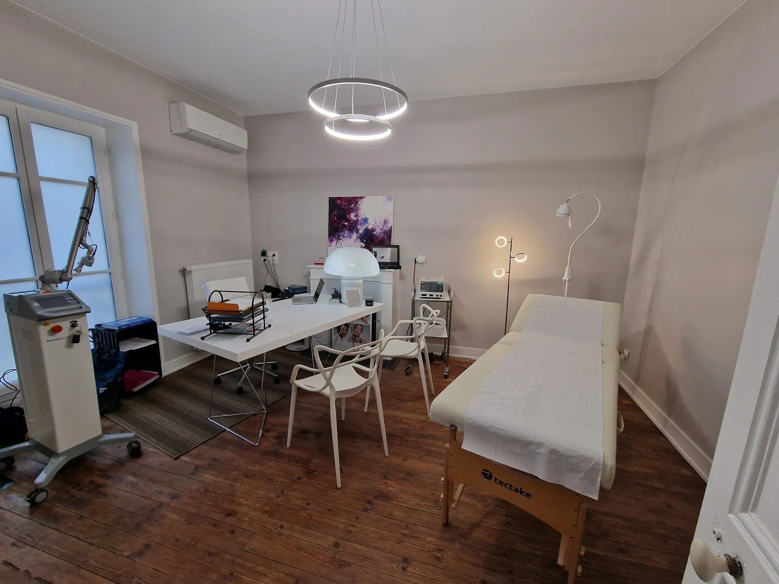 Salle de consultation du cabinet de Vésone à Périgueux : bureau blanc, table d’examen et appareil laser près de la fenêtre